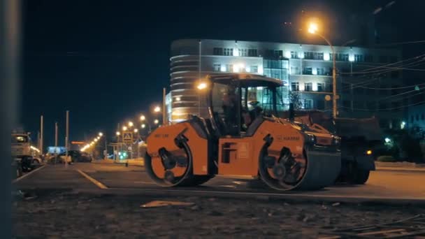 Novosibirsk regio, 7 september 2019. De roadroller staat tegen de achtergrond van nachtelijke stadsverlichting. Reparatie van wegdek, verbetering. Uitrusting voor wegenbouw. — Stockvideo
