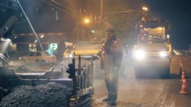 Novosibirsk bölgesi, 7 Eylül 2019. Asfalt kaldırım kontrol panelinde yol işçisi. Sıcak asfalt karışımından buhar. Arka planda, iki silindirli asfalt seriyor.