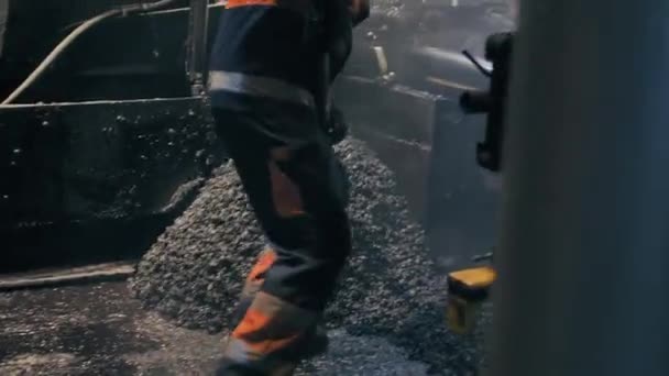 Los trabajadores del camino extienden el asfalto con una pala delante de una pavimentadora de asfalto. Reparación de una carretera de la ciudad por la noche. Trabajos de construcción de carreteras. — Vídeo de stock