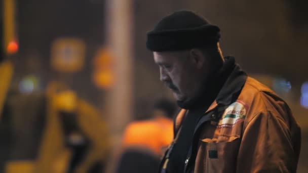 Novosibirsk região, 7 de setembro de 2019. Close-up é um trabalhador rodoviário de meia-idade. Um rolo de estrada está trabalhando no fundo. Um homem de uniforme. Reparação de uma estrada de cidade à noite. — Vídeo de Stock