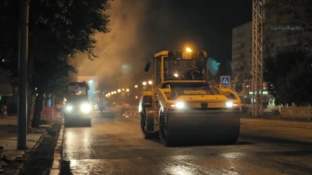 Novosibirsk region, 2019 년 9 월 7 일. 두 대 의도 로 로울러 가 그 도시 의 아스팔트 를 부순 것이다. 뜨거운 아스팔트에서 나온 증기입니다. 밤에 도로 보수. — 비디오