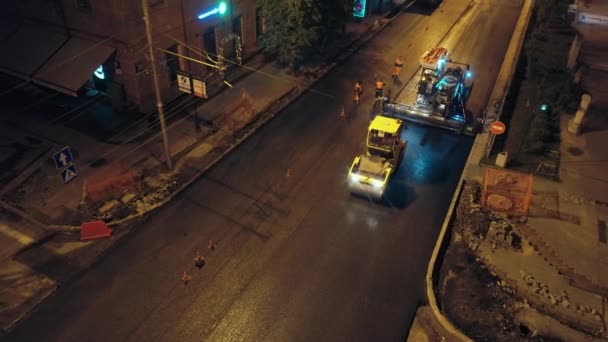 Gebiet Nowosibirsk, 7. September 2019. Luftaufnahme. Eine Straßenwalze legt Asphalt vor der Lichterkulisse der Stadt. Der Asphaltfertiger ist in Betrieb. Straßenreparaturen in der Stadt. — Stockvideo