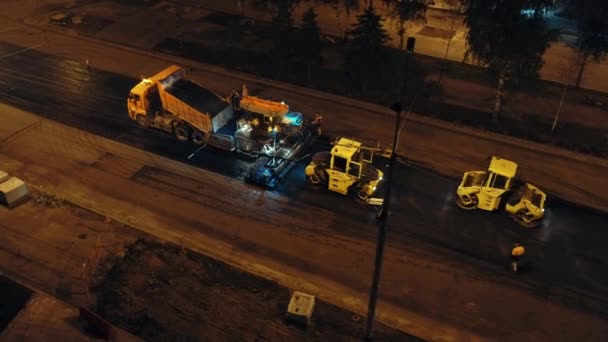 Hava görüntüsü. Bir çöp kamyonundan asfalt beton karışımını asfalt kaldırıma boşaltma hazırlığı. Asfaltı döşeyen iki yol silindiri. Şehirde yol tamiri. Yol işçileri. — Stok video