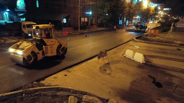 Novosibirsk region, 2019 년 9 월 7 일. 공중에서 본 모습. 도로 로울러 는 도시의 조명등 뒤쪽에 아스팔트 를 놓는다. 아스팔트 주조기가 작동하고 있습니다. 밤에 도시에서 도로를 보수하는 모습. — 비디오