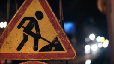 Close-up of a road sign warning drivers about road works. Grunge road traffic sign. Signal lights flash in the background.
