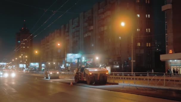 Obwód nowosybirski, 20 maja 2021 r. Dwie rolki drogowe układają asfalt na tle miasta w nocy. Samochody jadą przodem. Światła nocnego miasta. Naprawa dróg. — Wideo stockowe