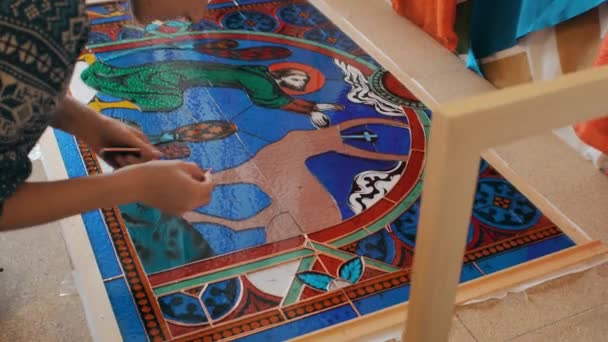 Novoszibirszk régió, 2020. szeptember 18. A művész összegyűjti a festett üvegmozaik részleteit. Kézzel készített. Foltos üvegműhely. — Stock videók