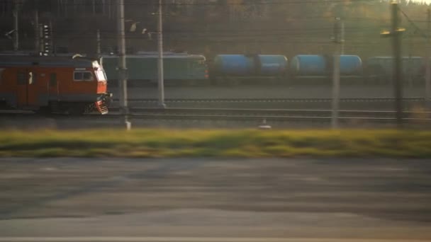 Pociąg odjeżdża o zachodzie słońca. Lokomotywa elektryczna w pięknym słońcu. Pociąg na tle pociągów i lasów. — Wideo stockowe