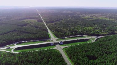 Hareket halindeki araba ve kamyonlarla kavşağın hava görüntüsü. Nakliye kavşağı, kozalaklı bir ormanda yol. Yaz güneşli bir gün.