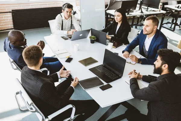 Grupo de jóvenes empresarios que trabajan y se comunican sentados en el escritorio de la oficina junto con sus colegas sentados. reunión de negocios — Foto de Stock