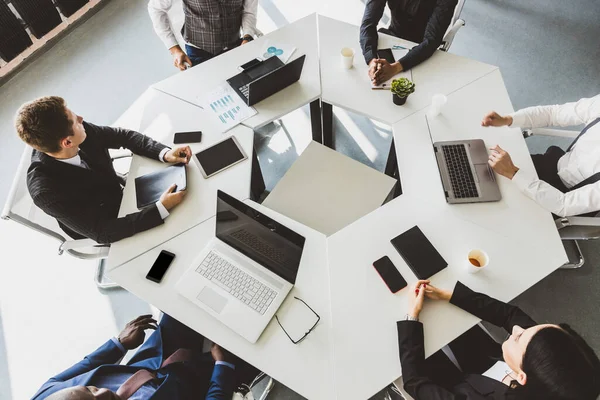 Grupo de jóvenes empresarios que trabajan y se comunican sentados en el escritorio de la oficina junto con sus colegas sentados. reunión de negocios. Escritorio vista superior. — Foto de Stock