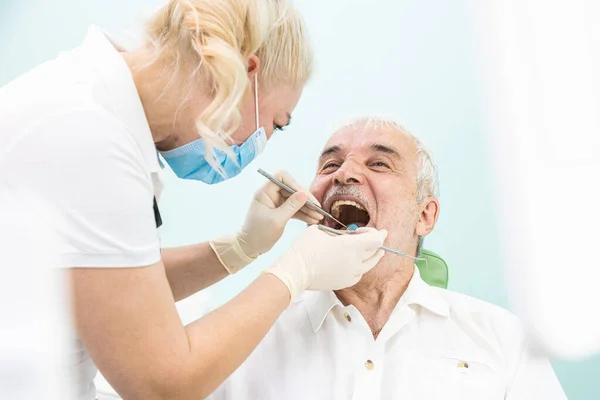 Conceito de Odontologia. Serviços odontológicos profissionais e equipamentos modernos sem dor. O médico consulta um paciente idoso do sexo masculino e examina os dentes e cavidade oral — Fotografia de Stock