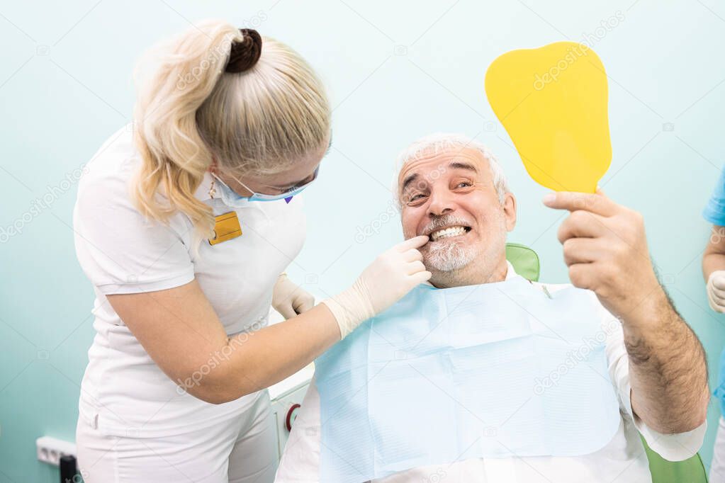 Dentistry concept. Professional dental services and modern equipment without pain. A doctor consults and treats an elderly man. The patient looks in the mirror