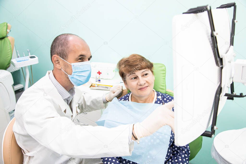 Dentistry concept. Professional dental services and modern equipment without pain. The doctor consults and treats an elderly woman and shows the results on the monitor