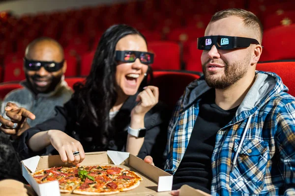 Los amigos ven una película en el cine, comen pizza y se ríen. La gente se sienta en los sillones del cine y mira la pantalla — Foto de Stock