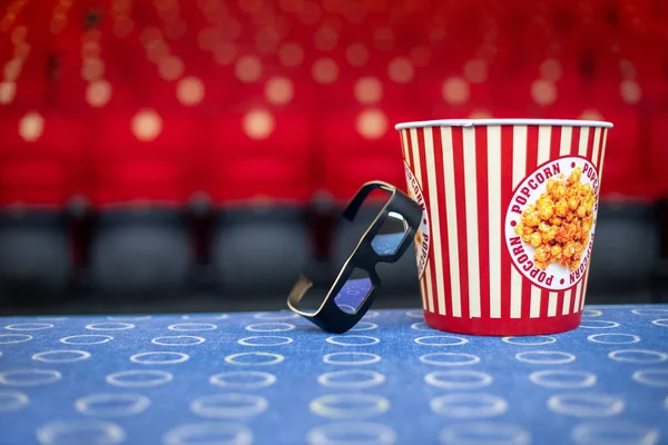 Un gran cubo de palomitas de maíz y vasos 3D en el fondo de las sillas de cine — Foto de Stock