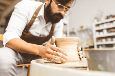 Genç bir erkek çömlekçi atölyesinde çömlekçi çarkında el işi yapıyor ve kilden bir ürün yapıyor.