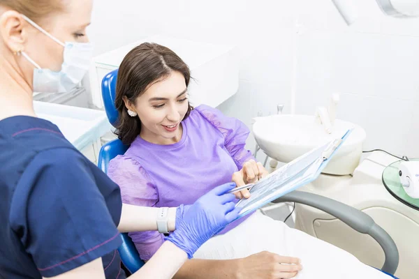 Il concetto di odontoiatria. Servizi odontoiatrici professionali e attrezzature moderne senza dolore. Il medico consulta e tratta la giovane donna, conduce un esame e redige un piano di trattamento. — Foto Stock