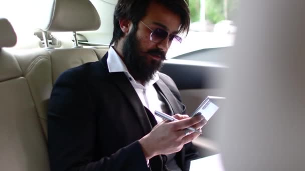 Стильный индийский бизнесмен в машине работает и пользуется смартфоном. Бизнес-вызовы и мобильность в совместном процессе — стоковое видео