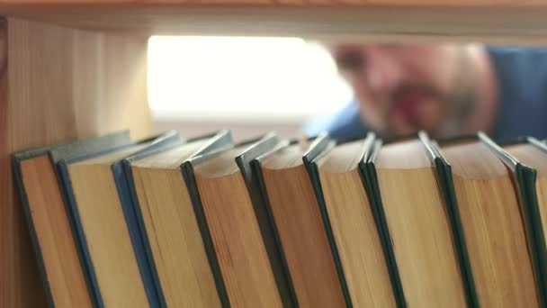 Un hombre toma un libro de una estantería de cerca. Vista interior de un estante — Vídeo de stock