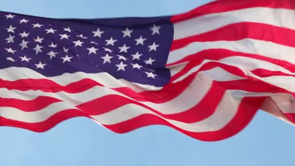 Gran bandera nacional americana ondeando en el viento sobre un asta de la bandera contra un cielo azul de cerca — Vídeo de stock