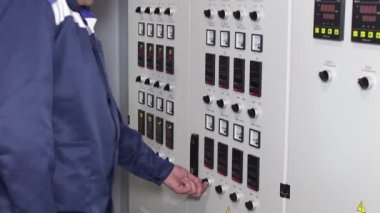 Fabrikadaki elektrik kontrol odasının yanındaki erkek fabrika işçisi. Sayısal göstergeler ve düğmeler