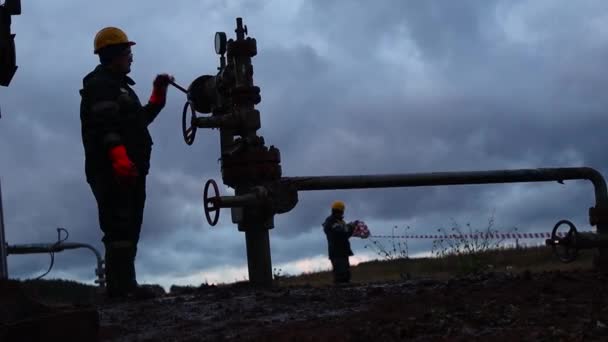 An employee in overalls and a helmet is carrying out repairs and maintenance of an oil well. Silhouette on the background of the evening sky — Stock Video