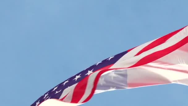 Μεγάλη αμερικανική εθνική σημαία κυματίζει στον άνεμο σε ένα κοντάρι σημαίας σε ένα μπλε ουρανό από κοντά — Αρχείο Βίντεο