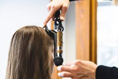 Usta kadın kuaför bir güzellik salonunda saç kıvıran kızı nazikçe kıvırtır. Saç şekillendirme