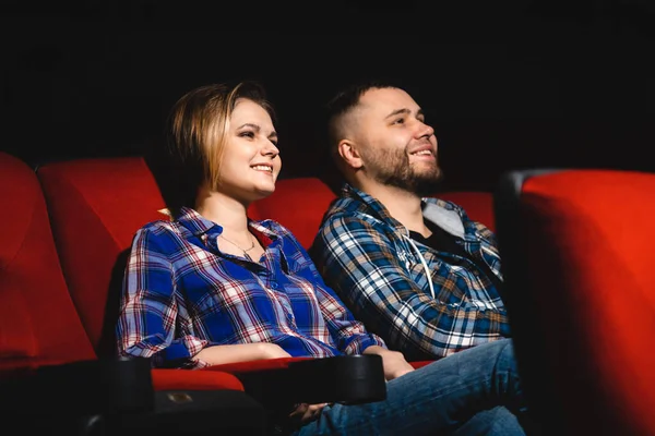 Friends are watching a movie in the cinema. People sit in the armchairs of the cinema and look at the screen