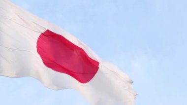 Japonya 'nın ulusal bayrağı mavi gökyüzüne karşı bir bayrak direğinde rüzgarda sallanıyor.