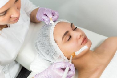 Yüz bakımı ve korunma. Güzellik uzmanıyla randevusu olan genç bir kadın. Uzman yüzüne krem maske takıyor.