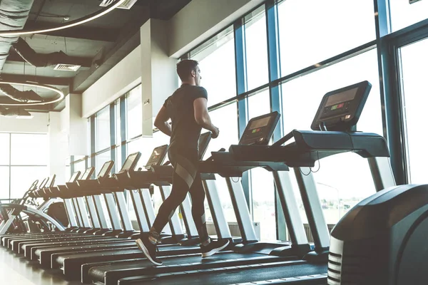 Modern spor salonundaki koşu bandında koşan siyah spor giysili bir sporcu.