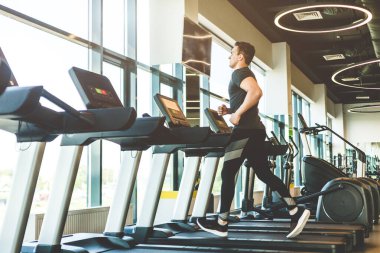 Modern spor salonundaki koşu bandında koşan siyah spor giysili bir sporcu.