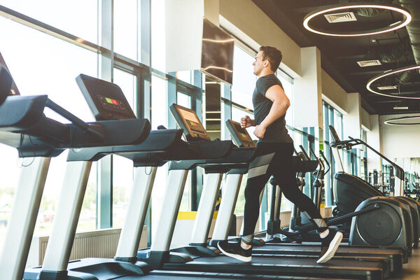 Спортсмен, одетый в черное спортивное платье, бежит по беговой дорожке в современном спортзале