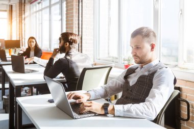 Gündelik giyinen genç iş adamları ofiste birlikte çalışıyorlar. Ekip iş başında.