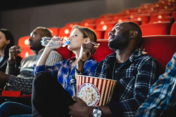 Friends watching a movie in the cinema with popcorn. People sit in the armchairs of the cinema and look at the screen