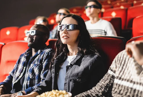 Friends are watching a movie in the cinema. People sit in the armchairs of the cinema and look at the screen with special glasses for 3D