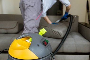 Temizlik servisi. Eldivenli ve elektrikli süpürgeli adam. Profesyonel ekipmanlı temiz kanepe.