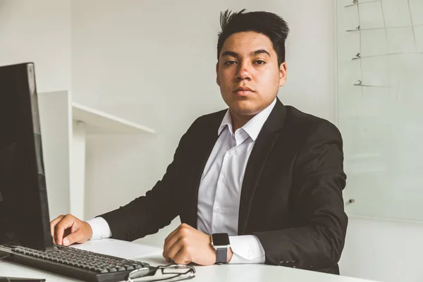 Een jonge kantoormedewerker zit achter een bureau, met behulp van een computer. Twee zakenmannen aan het praten. — Stockfoto