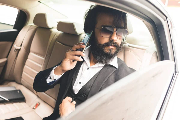 Elegante guapo Seo Hindu con gafas y una barba está hablando por teléfono en el asiento trasero del coche. Viajes de negocios seguros y cómodos — Foto de Stock