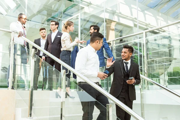 Jóvenes empresarios arego abajo de las escaleras y hablando en el fondo de las oficinas de vidrio. Corporativossteam y gerente en una reunión. — Foto de Stock