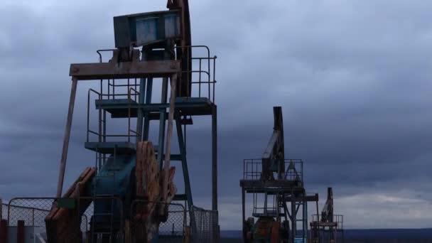 Zuigerstangpompen werken en pompen olie tegen de achtergrond van de avondlucht. Dienst olieboorputten — Stockvideo