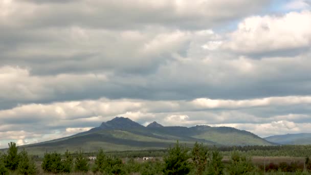 Timelapse tjocka moln flyter över en grön bergstopp och en vacker vintergrön nationalpark — Stockvideo