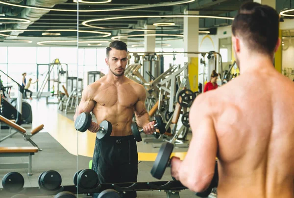 Atlético homem fazendo dumbbell exercício na frente de um espelho nu torso no ginásio — Fotografia de Stock