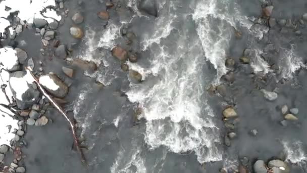 Closeup view of above a mountain river running over stones. The camera descends to a cold, shallow mountain stream. A stormy stream flowing through the stones — Vídeos de Stock