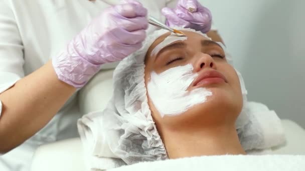 Gesichtspflege und -schutz. Eine junge Frau bei einem Kosmetiktermin. Der Spezialist trägt eine Crememaske auf das Gesicht auf — Stockvideo