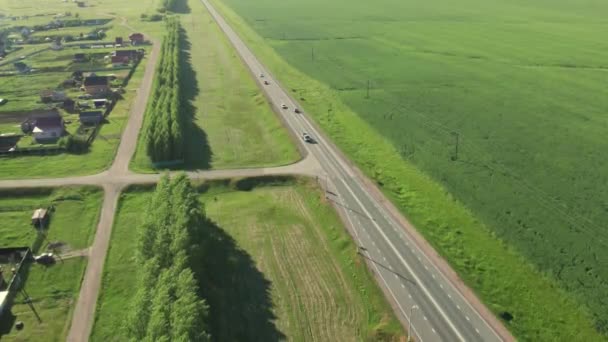 Вид с воздуха на шоссе с автомобилями и грузовиками, проходящими вдоль небольших деревень и зеленых полей и лугов. — стоковое видео