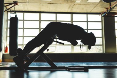Pencerenin karşısındaki spor salonunda genç bir adam antrenman yapıyor. Karın egzersizi.