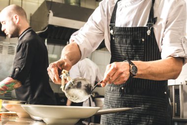 Oteldeki mutfak restoranında yemek pişiren profesyonel bir aşçı. Yemek hazırlıyor. Önlüklü bir aşçı sebze ve pizzadan salata yapar..